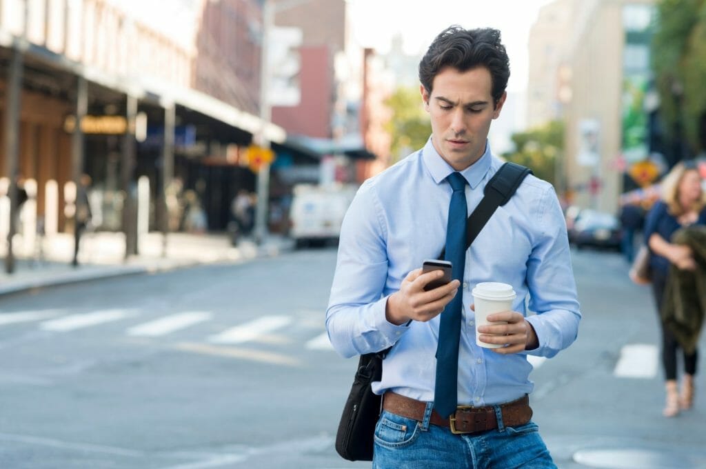 Man on phone holding coffee and walking through the streets