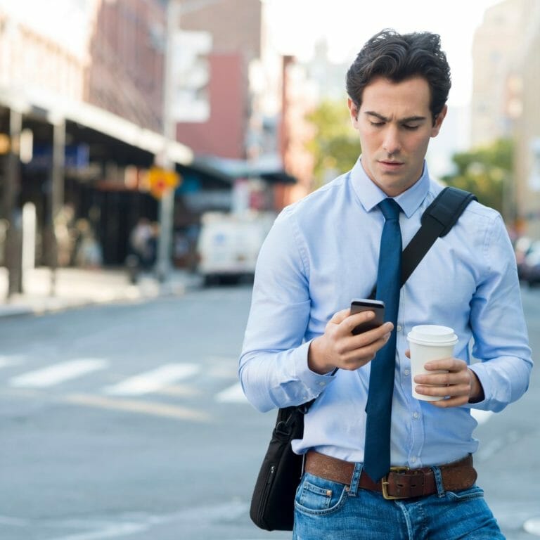 Man on phone holding coffee and walking through the streets