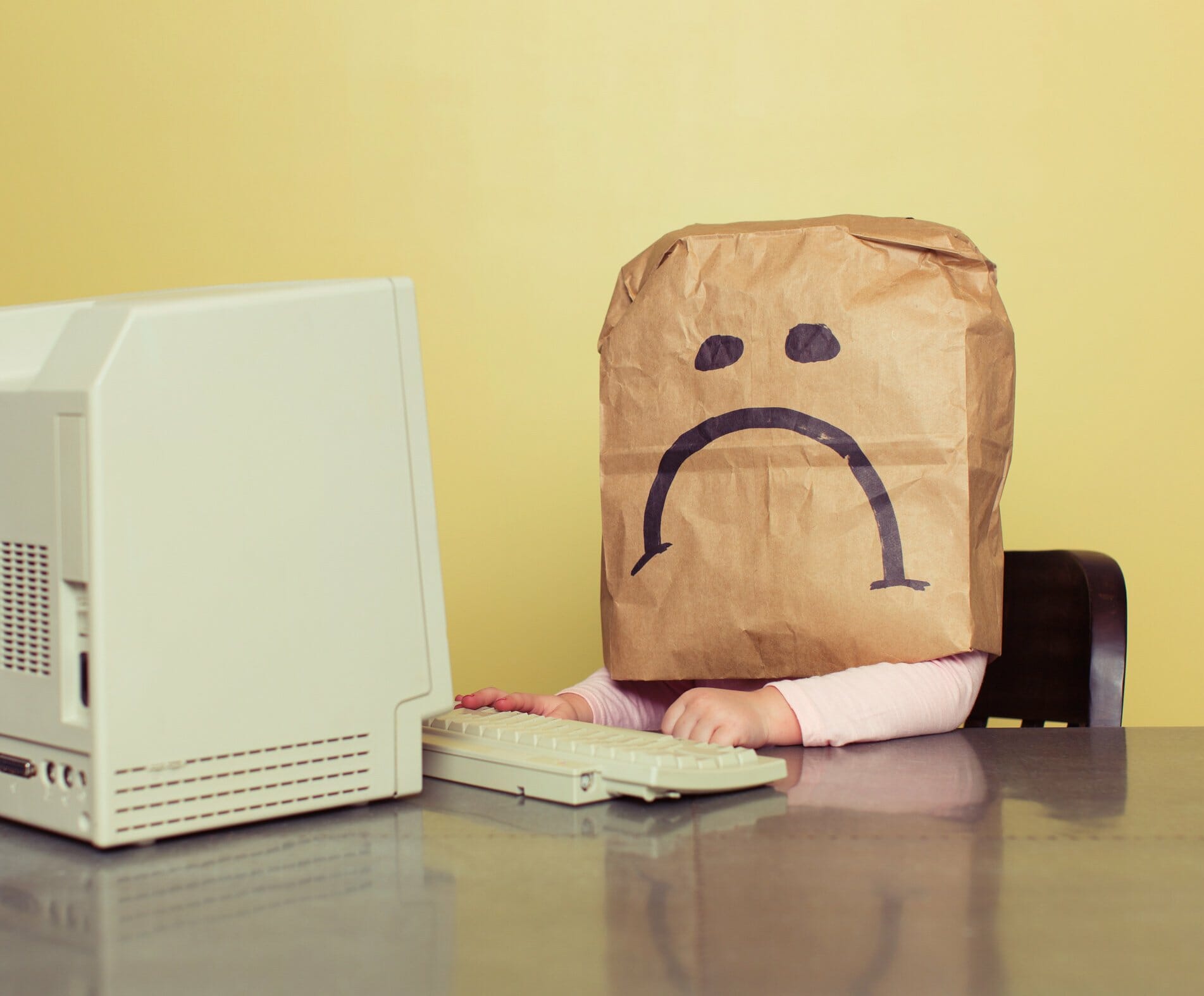 Employee with paper bag with sad face drawn on over their head