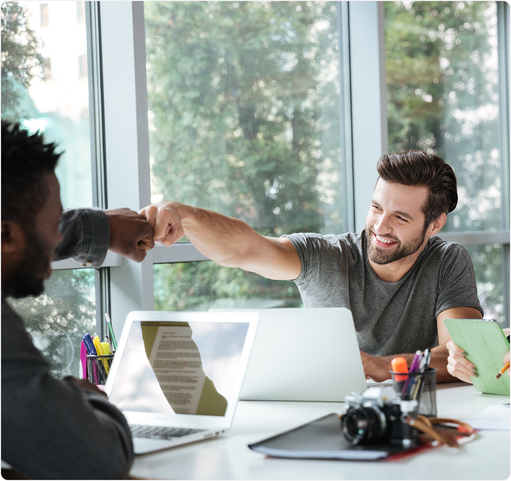 Two co-workers in an office are giving each other a fist bump. 