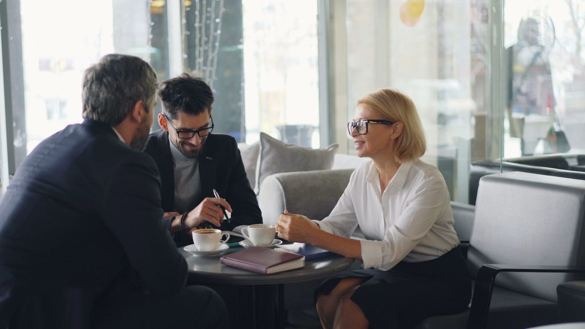 A PI Certified Partner meets with two clients over coffee in a café.